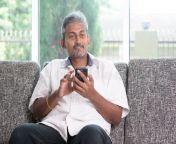 indian guy using smartphone mobile apps concept mature mobile phone asian man relaxed sitting sofa indoor 57307121.jpg from old indian guy using mobile cam in ba