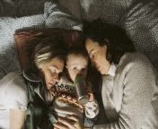 girl drinking milk while lying amidst lesbian mothers on bed at home masf24736.jpg from mom lesbians milk sleebing feeding