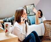 teenage girl using mobile phone while her friend laying bed reading book relaxing young friends home brother sister adolescence enjoy family time room 6602 665.jpg from sis her friend call home pr koi nahi h home pr aaja