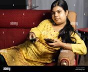 an indian housewife woman watching television holding remote and mobile phone in hands sitting on sofa 2g92yp3.jpg from aunty remote image