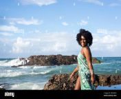 beautiful smiling woman with black power hair wearing light green outfit with white bikini standing on the rocks of a beach blue sky and clouds in th 2rdx4ph.jpg from bikini batu ebony